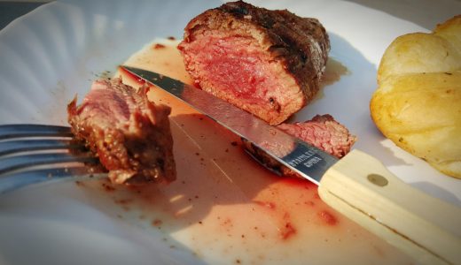 黒い手袋の入れ墨された肉屋の手は、カメラでジュースや血と染色器で新鮮な生肉の一部を提供します無料写真